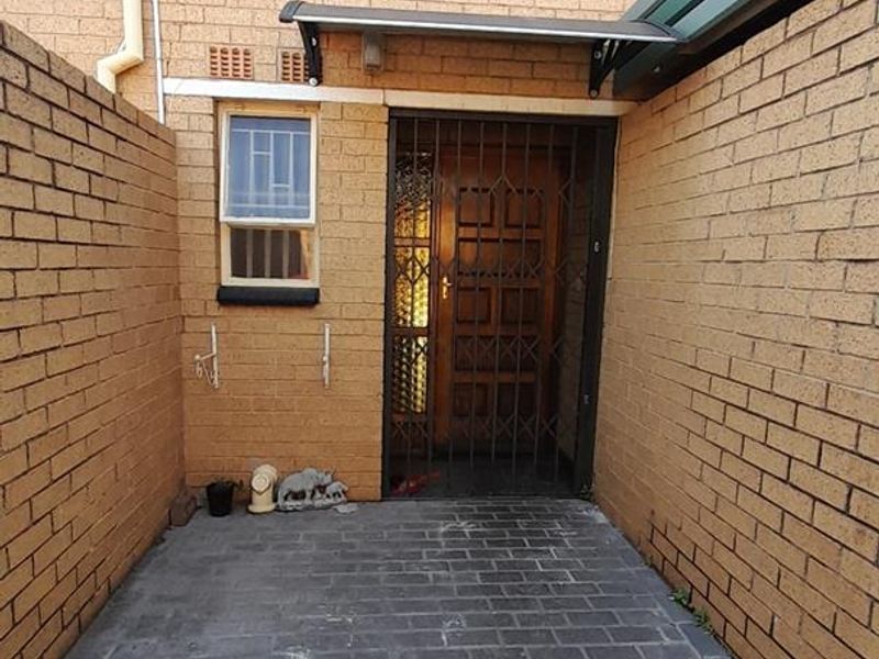 A private paved entrance courtyard featuring face-brick walls, a secure metal gate, and a protective awning over the main doorway.