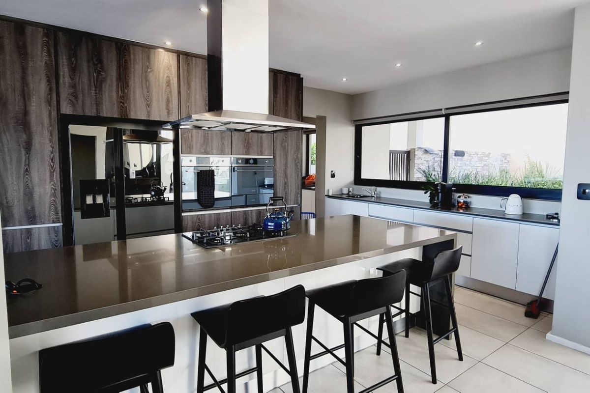 Modern kitchen featuring a large central island with gas hob, integrated appliances, sleek cabinetry, and stone countertops, illuminated by recessed lighting.