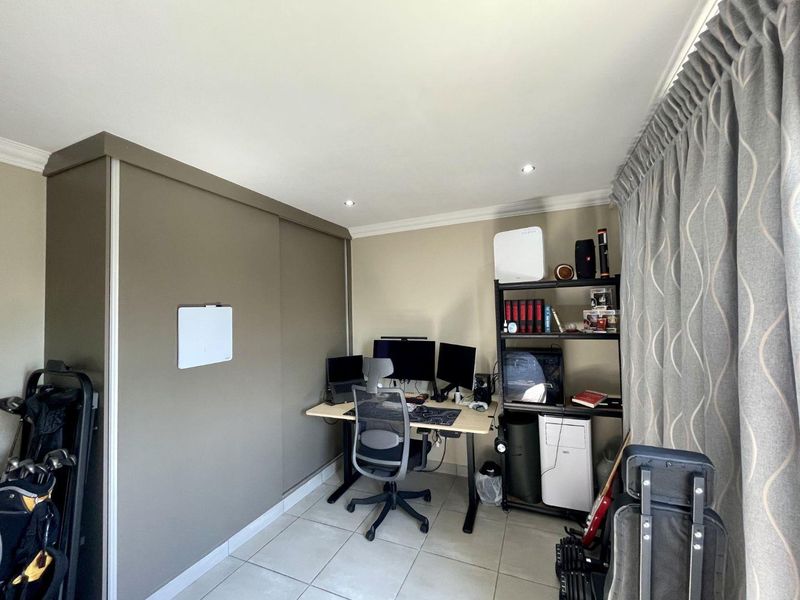 A functional home office space featuring tiled flooring, recessed downlighting, and a large built-in sliding door wardrobe for storage.