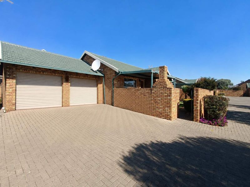 Front view of a townhouse featuring a double garage, paved driveway, and face-brick exterior with a tiled roof.