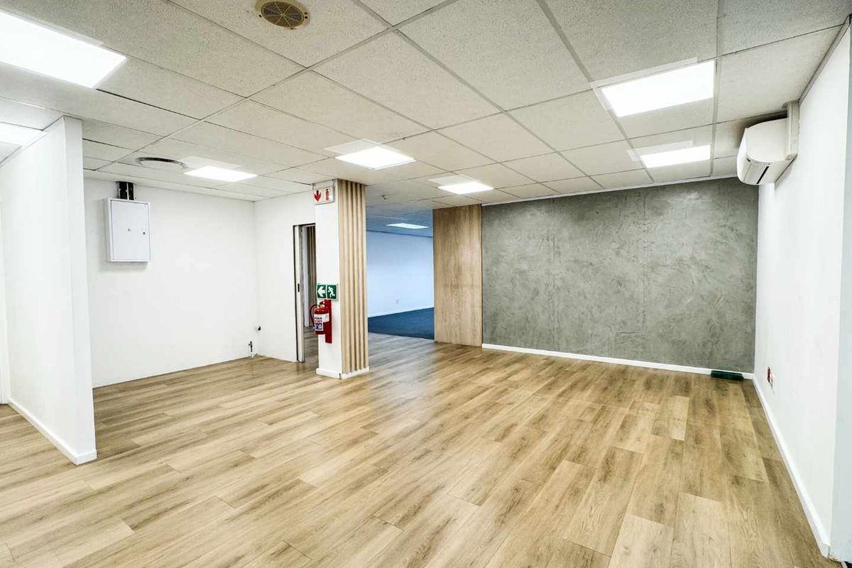 A bright, modern open-plan office space featuring wood-look flooring, a suspended ceiling with LED lighting, and a contemporary textured feature wall.