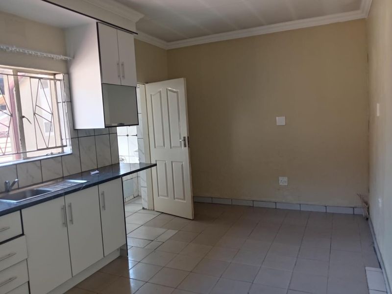 A functional kitchen featuring white built-in cabinetry, dark laminate countertops, a stainless steel sink, and tiled flooring, offering a clean, blank canvas for updates.