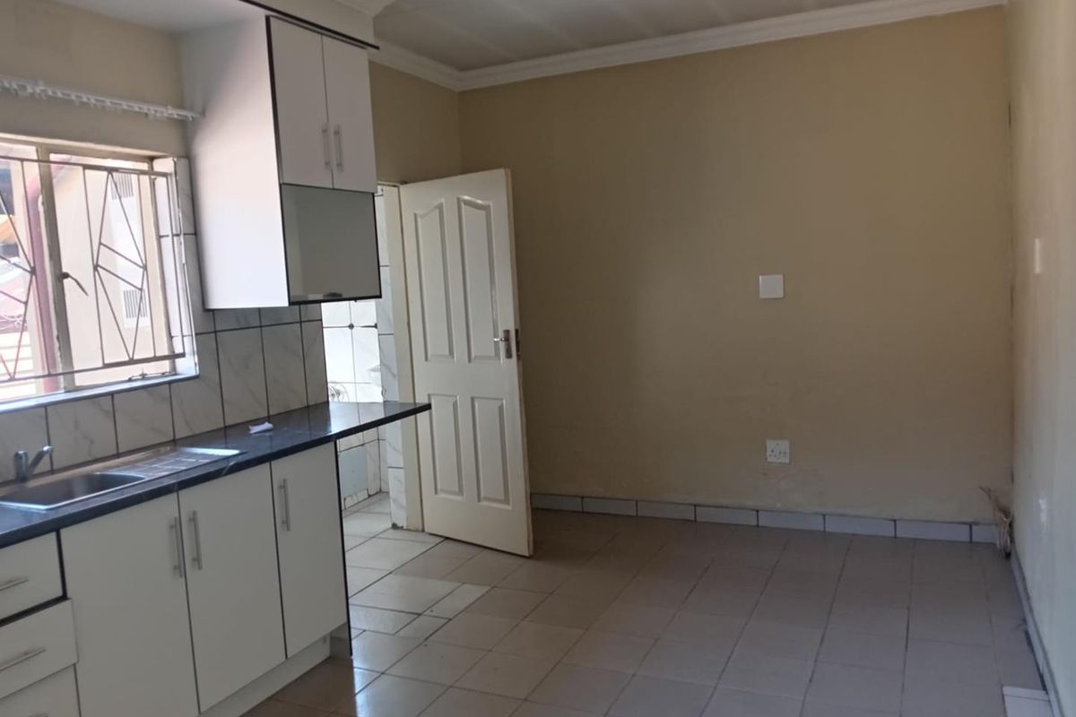 A functional kitchen featuring white built-in cabinetry, dark laminate countertops, a stainless steel sink, and tiled flooring, offering a clean, blank canvas for updates.