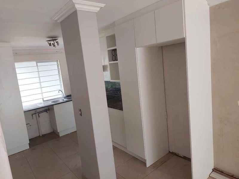 An empty kitchen area featuring white built-in cabinetry, a stainless steel sink, and tiled flooring, currently undergoing final finishing touches.