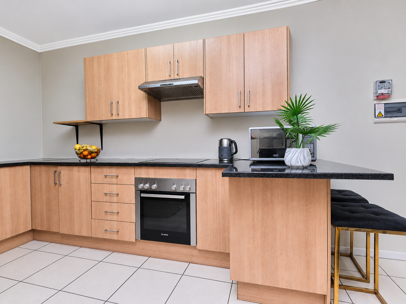 Modern kitchen featuring light wood cabinetry, granite countertops, built-in oven, electric hob, and tiled flooring with a breakfast bar extension.