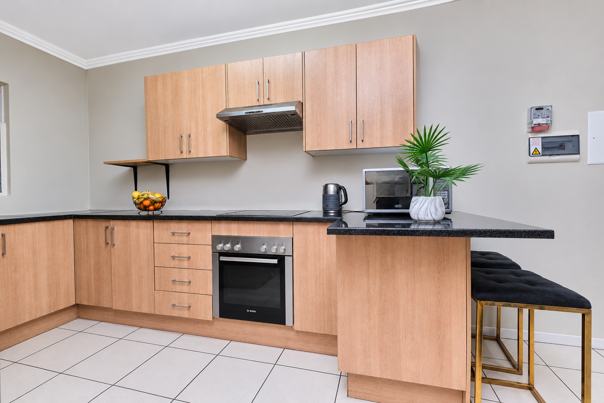 Modern kitchen featuring light wood cabinetry, granite countertops, built-in oven, electric hob, and tiled flooring with a breakfast bar extension.