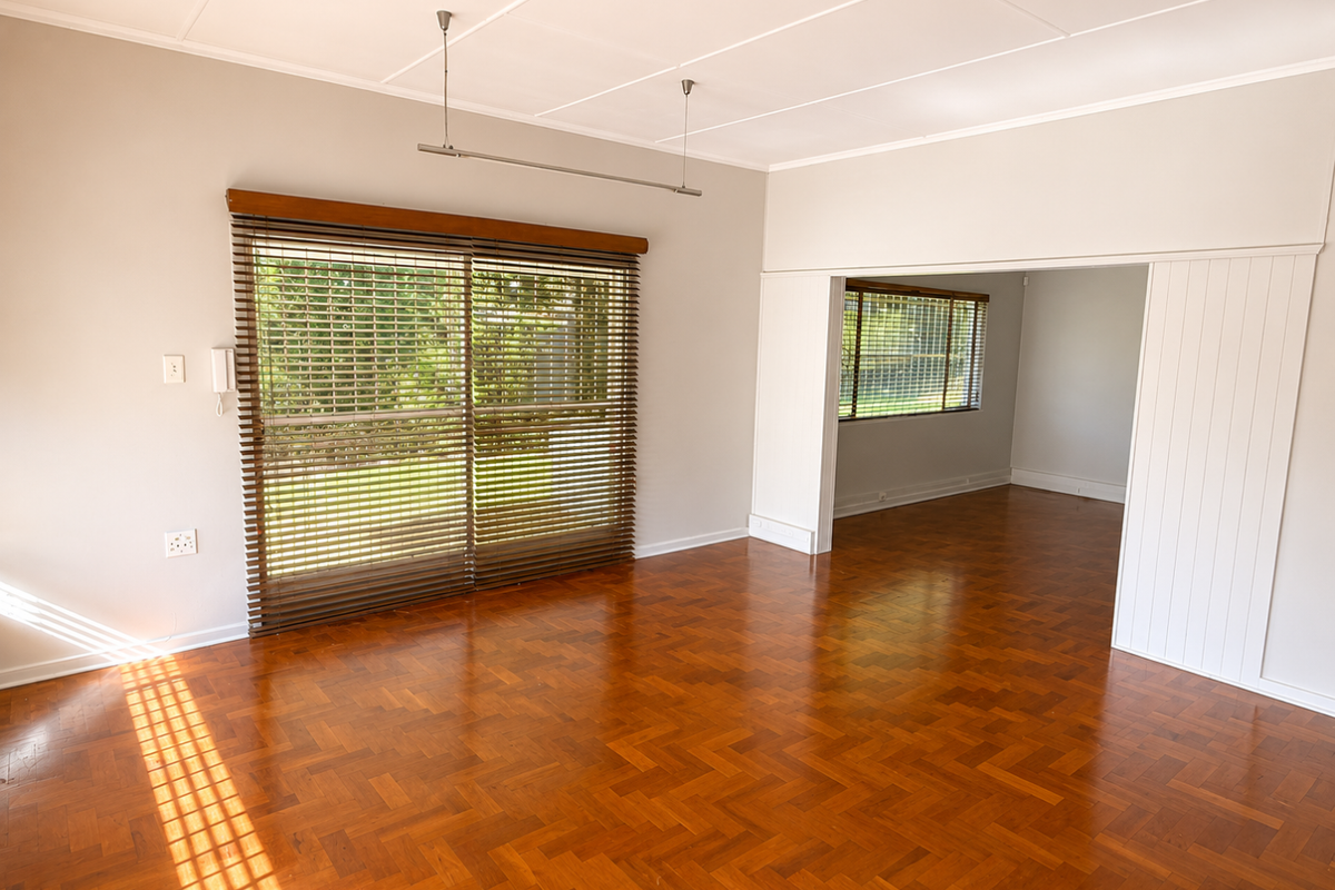 Spacious living area featuring polished parquet flooring, large sliding glass doors with timber blinds, and an open-plan layout connecting to an adjacent room.