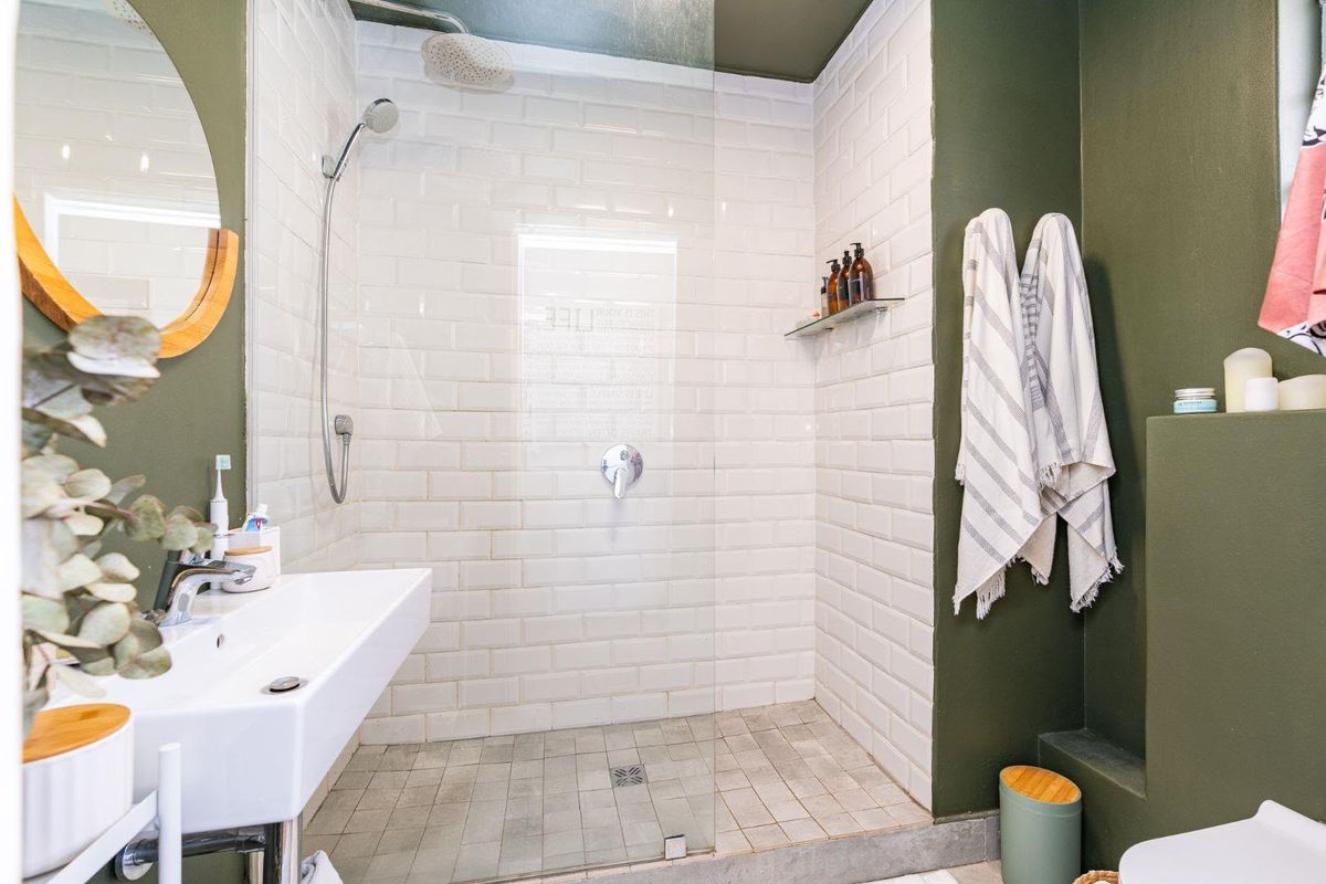 Modern bathroom featuring a walk-in shower with subway tiling, glass screen, and a sleek wall-mounted basin with olive green accent walls.