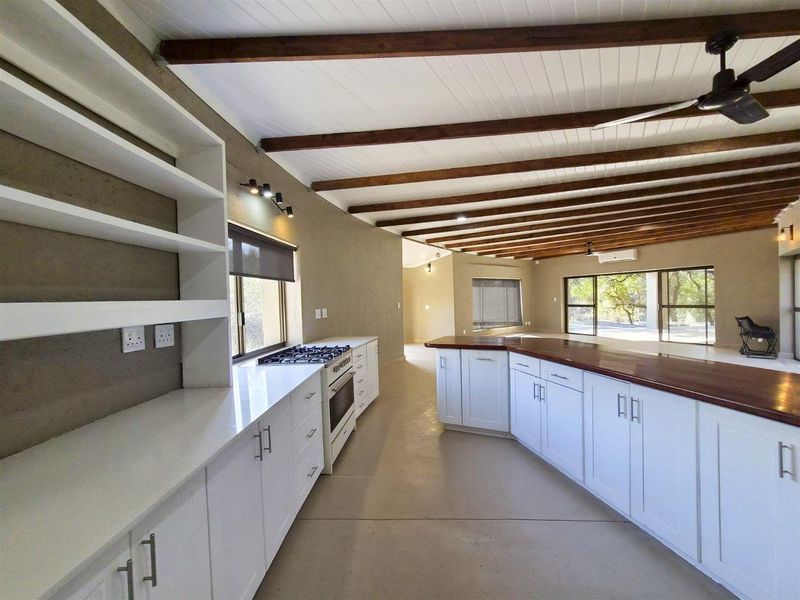 Spacious open-plan kitchen and living area featuring exposed timber ceiling beams, white cabinetry, stone and timber countertops, and large sliding doors to the exterior.