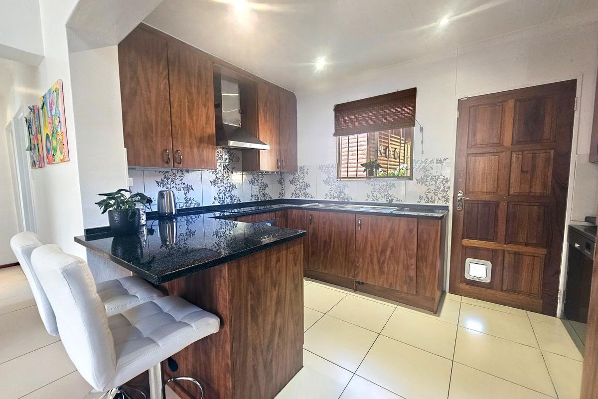 A functional kitchen featuring wood-finish cabinetry, dark granite countertops, a breakfast bar, tiled flooring, and a solid wood door with a pet flap.
