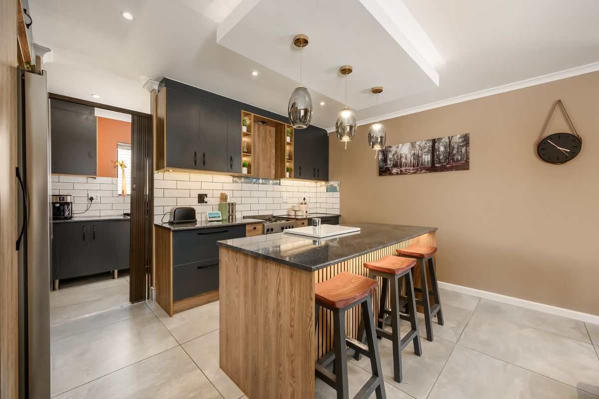 Modern kitchen featuring a central island with stone countertop, dark cabinetry, subway tile backsplash, and stylish pendant lighting, with an adjacent scullery area.