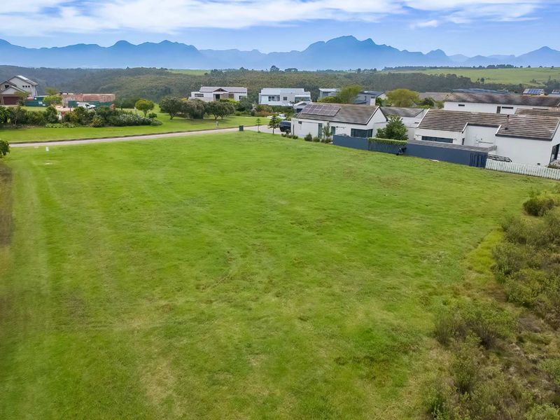 An aerial view of a vacant residential plot featuring a well-maintained grass lawn within a scenic estate setting with mountain views.
