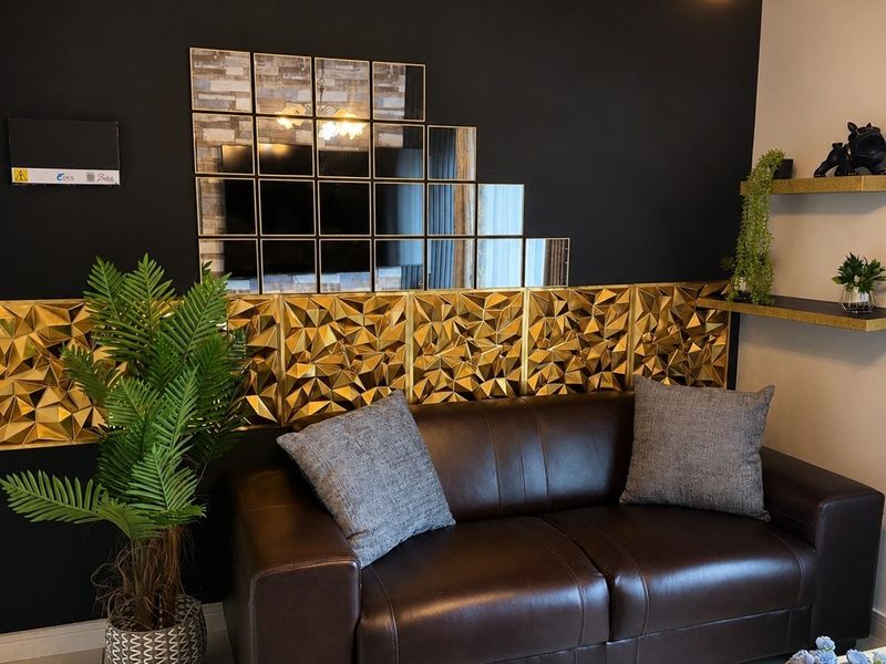 A living room featuring a dark accent wall with gold geometric paneling, decorative mirror tiles, and built-in shelving, complemented by tiled flooring.
