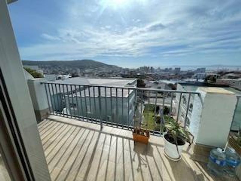 A balcony featuring tiled flooring and a metal balustrade, offering expansive elevated views of the surrounding urban landscape and distant hills.