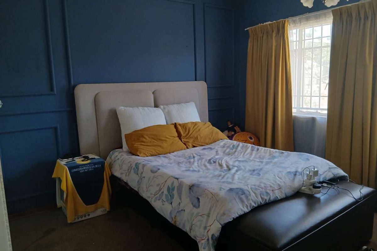 A bedroom featuring dark blue accent walls with decorative wainscoting and a window fitted with security bars.