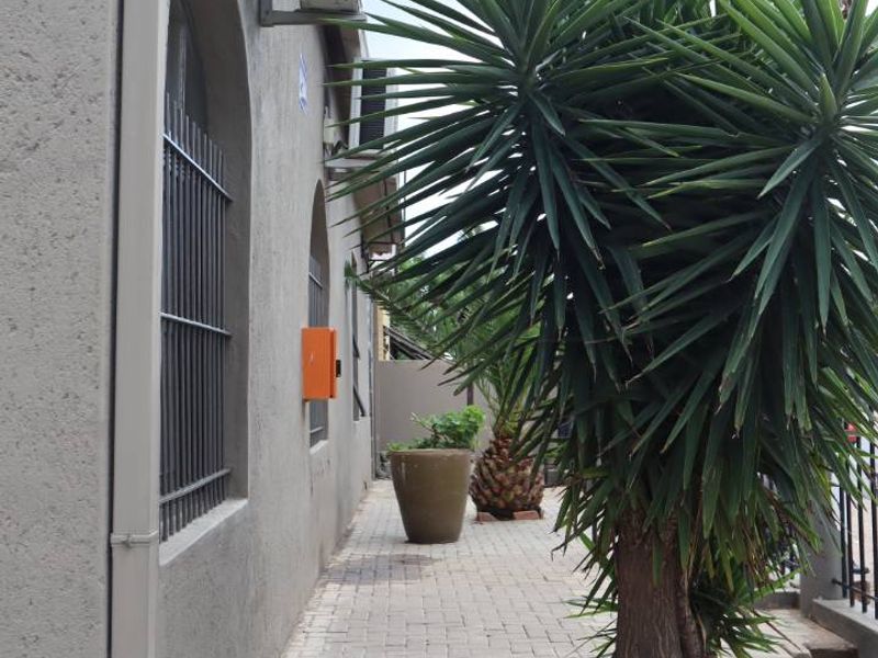 A paved side walkway featuring arched windows with security bars and an external air conditioning unit mounted on the building exterior.
