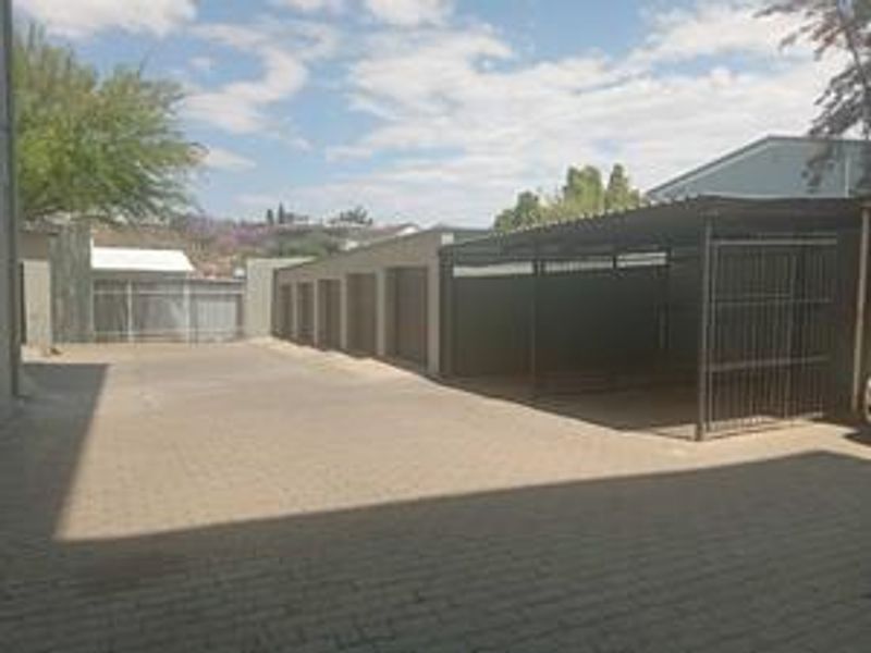 A paved parking area featuring a row of lock-up garages and a covered carport structure within a secure complex.