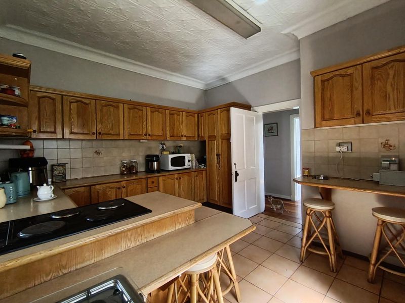A functional kitchen featuring traditional wooden cabinetry, laminate countertops, an integrated electric hob, and tiled flooring with a neutral backsplash.