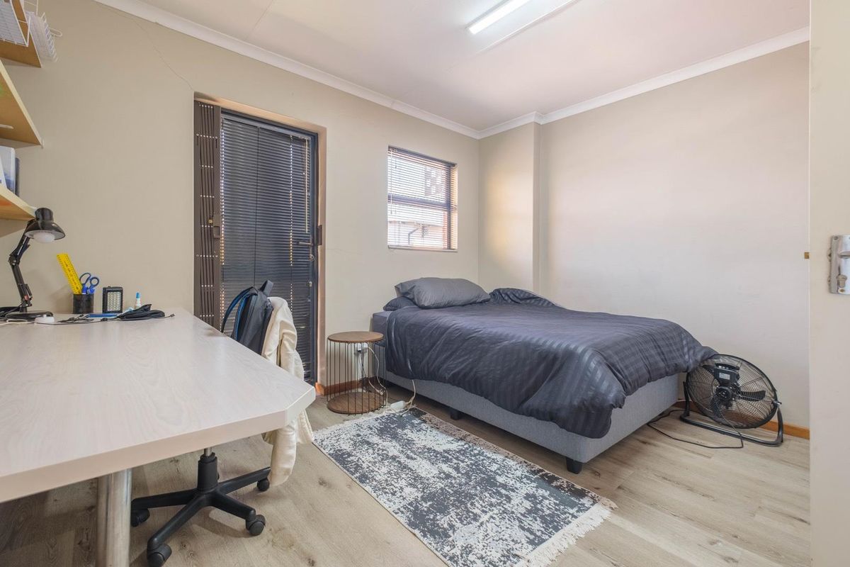 A functional bedroom featuring light wood-look flooring, a built-in desk area, and a glass-paneled door providing access to the exterior.