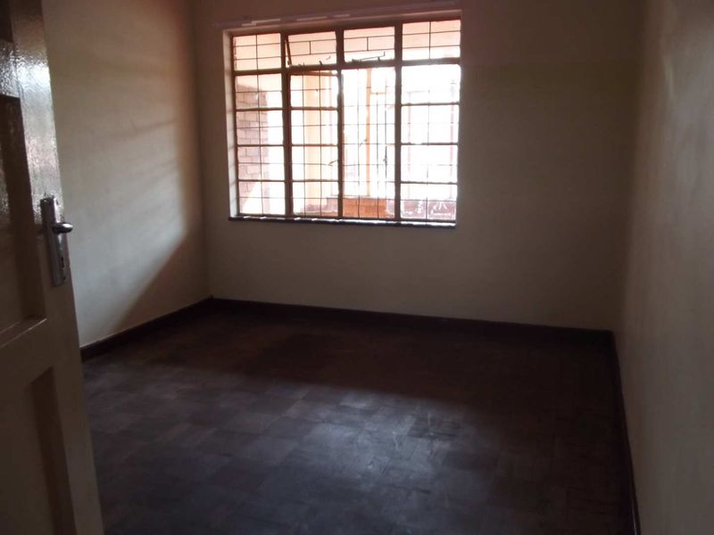 An empty bedroom featuring parquet flooring and a window fitted with metal security bars, offering a blank canvas for renovation.