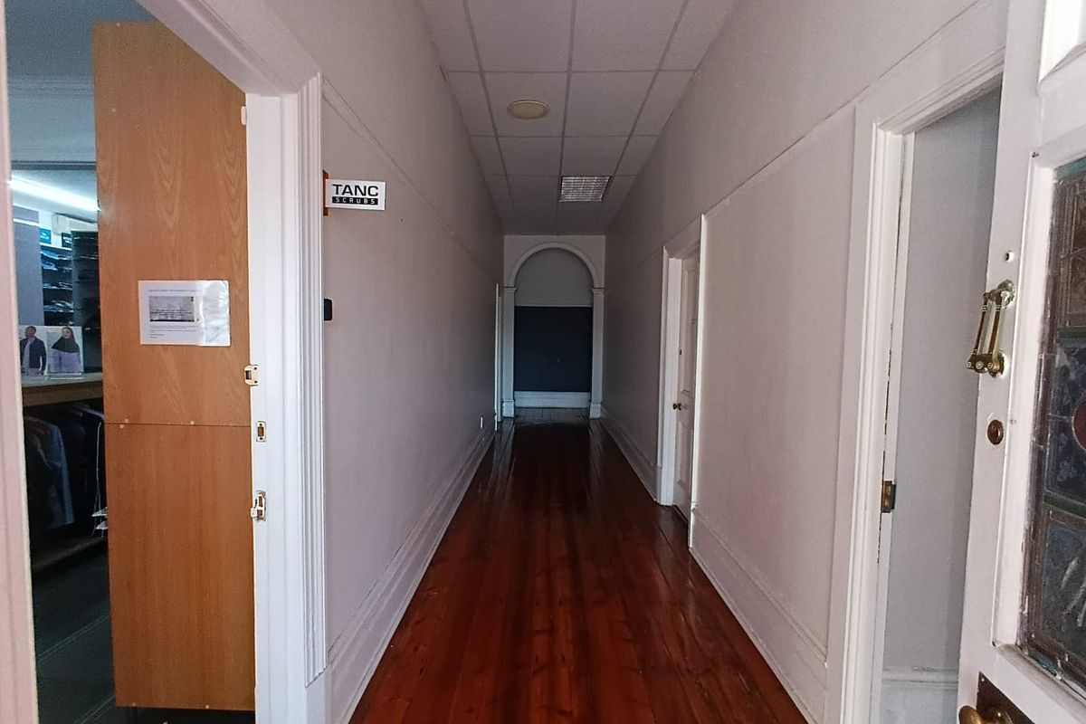 A long interior hallway featuring polished timber flooring, an arched transition, and a suspended ceiling with recessed lighting.