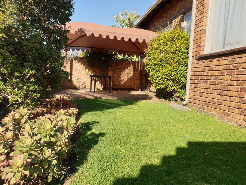 A private rear garden featuring a brick facade, a paved patio area with a canvas gazebo, and a well-maintained lawn.