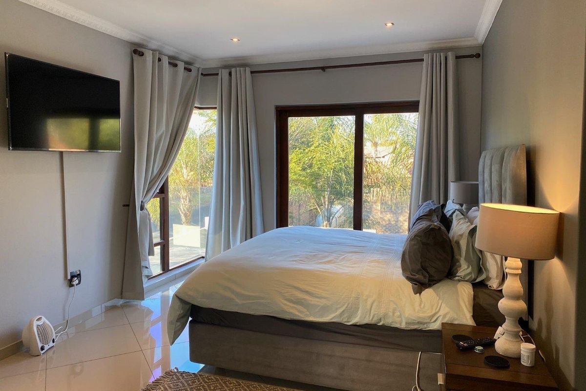 A well-maintained bedroom featuring tiled flooring, recessed downlighting, crown molding, and large sliding glass doors providing natural light and garden views.