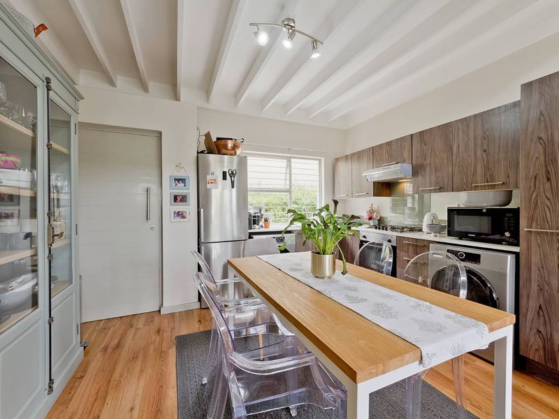 Modern open-plan kitchen and dining area featuring wood laminate flooring, exposed beam ceilings, contemporary cabinetry, and integrated appliances.