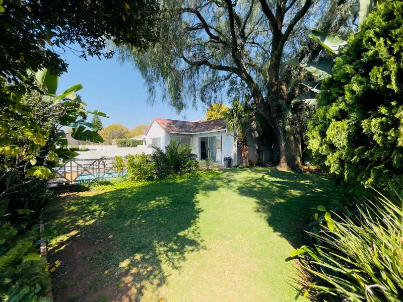 A view of the rear garden featuring a well-maintained lawn, mature trees, and a swimming pool adjacent to the main building structure.