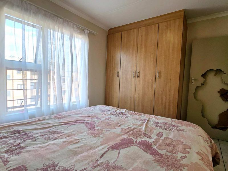 A bedroom featuring built-in wooden cupboards and tiled flooring, currently showing significant damage to the interior door.