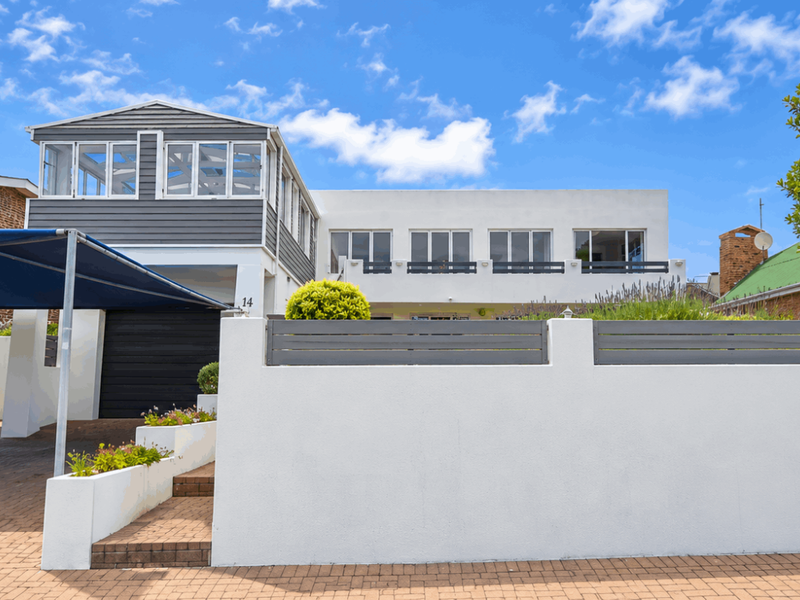 Front elevation of a multi-level house featuring a paved driveway, covered carport, and modern boundary wall with slatted fencing.