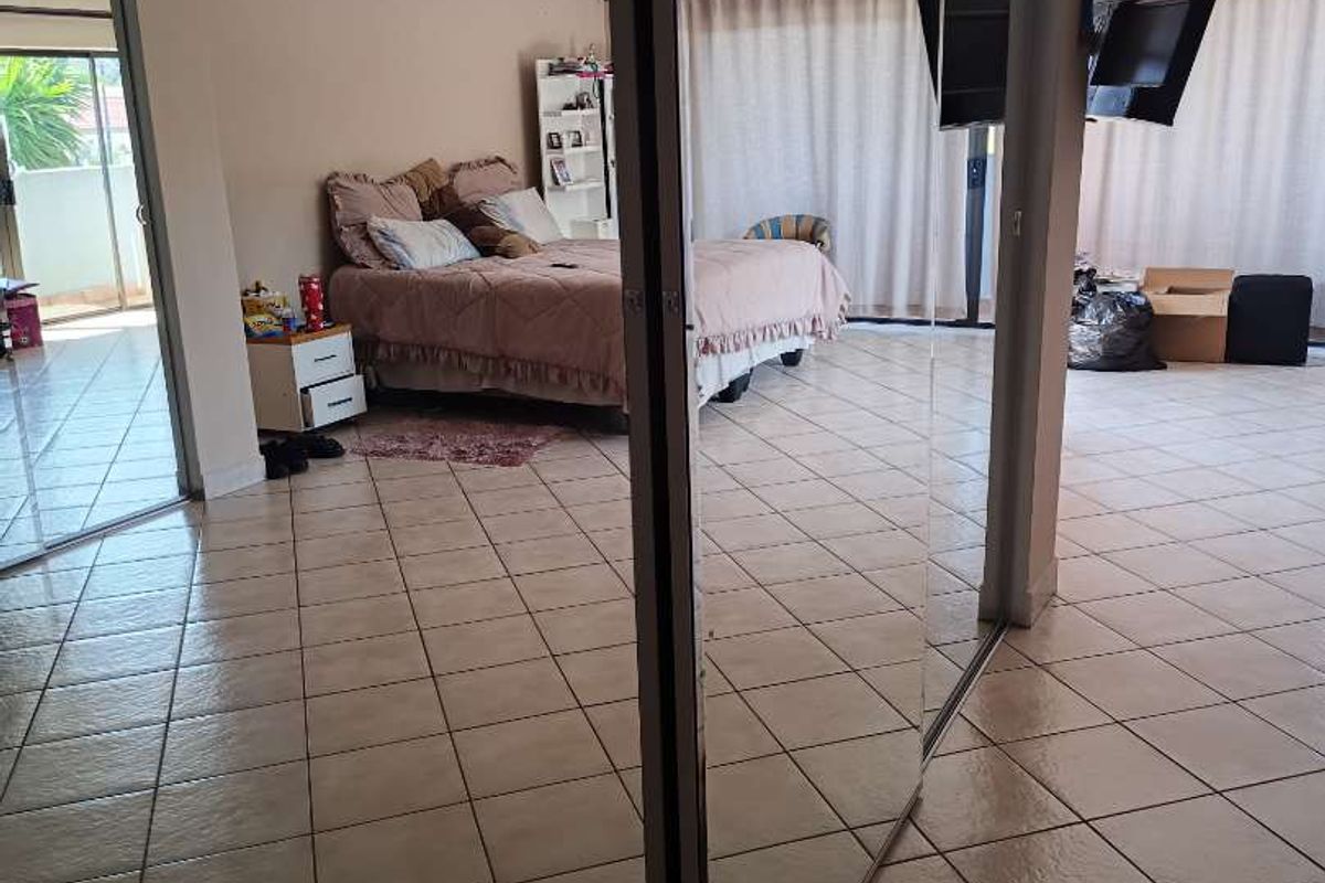 Spacious bedroom featuring tiled flooring, mirrored sliding wardrobe doors, and direct access to an outdoor balcony area through sliding glass doors.