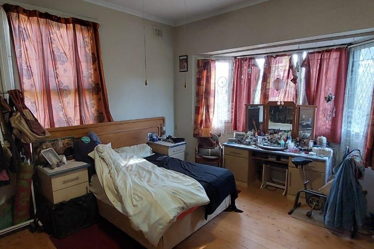 A spacious bedroom featuring timber flooring, large bay windows, and built-in cabinetry, offering a blank canvas for renovation and modernization.