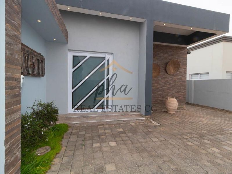 Modern front entrance featuring stone cladding, paved driveway, and recessed lighting, providing a contemporary and welcoming facade.