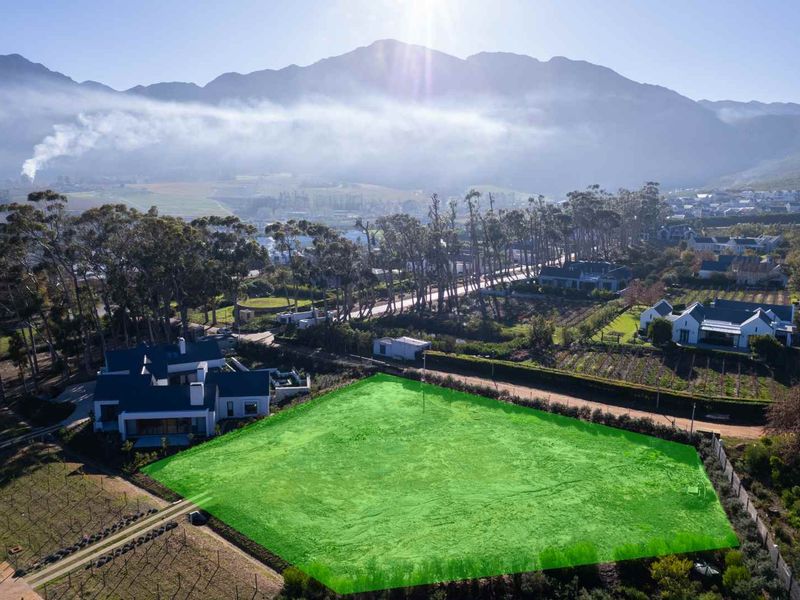 Aerial view of a vacant residential plot highlighted in green, situated in a scenic estate with mountain views and surrounding established homes.