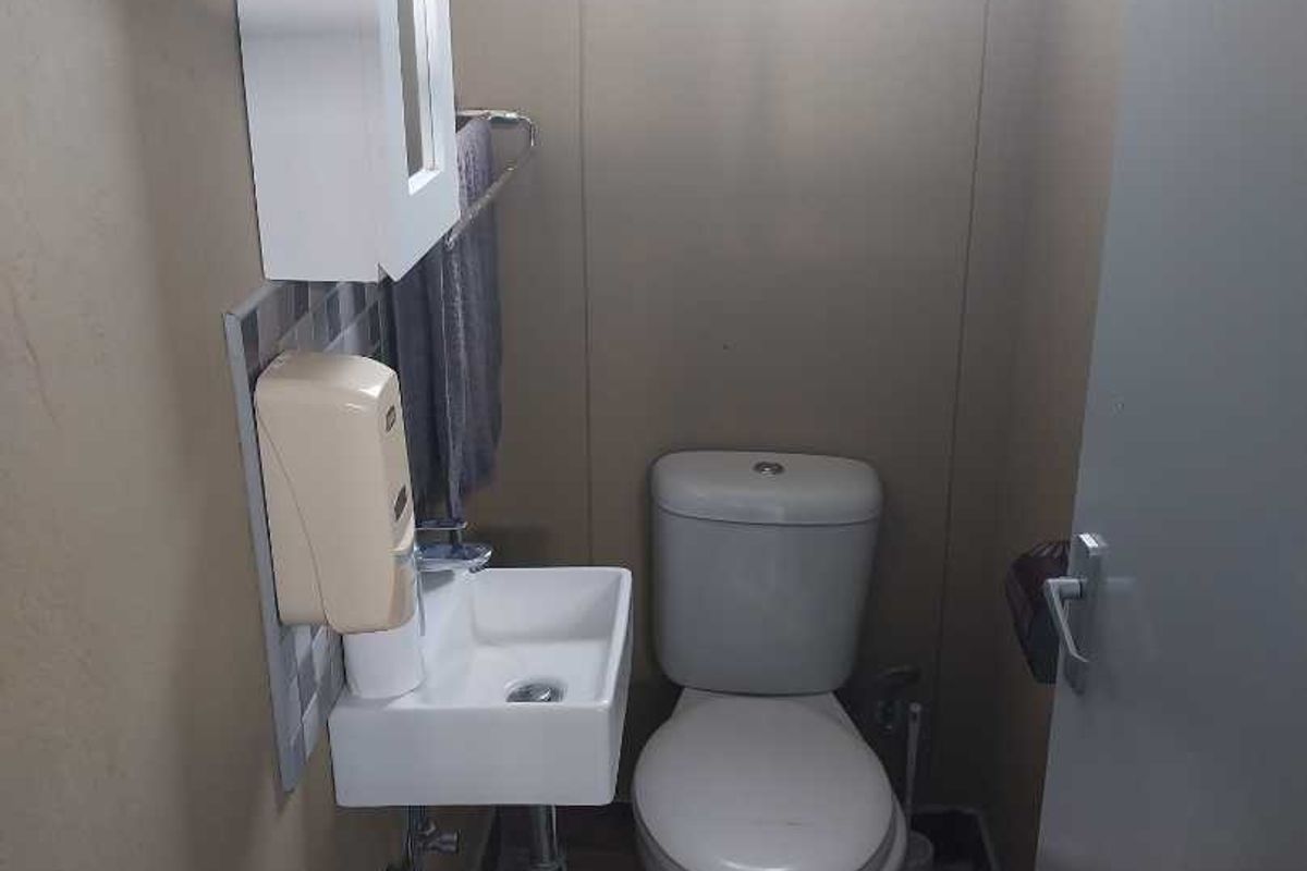 A compact office restroom featuring a wall-mounted basin, a standard toilet, and a small medicine cabinet.