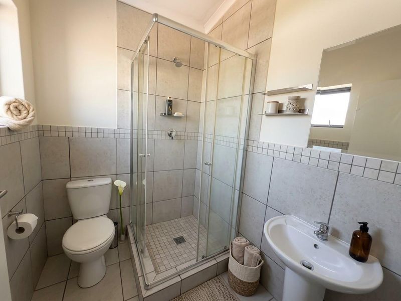 A clean and functional bathroom featuring a glass shower enclosure, pedestal basin, toilet, and neutral wall tiling.