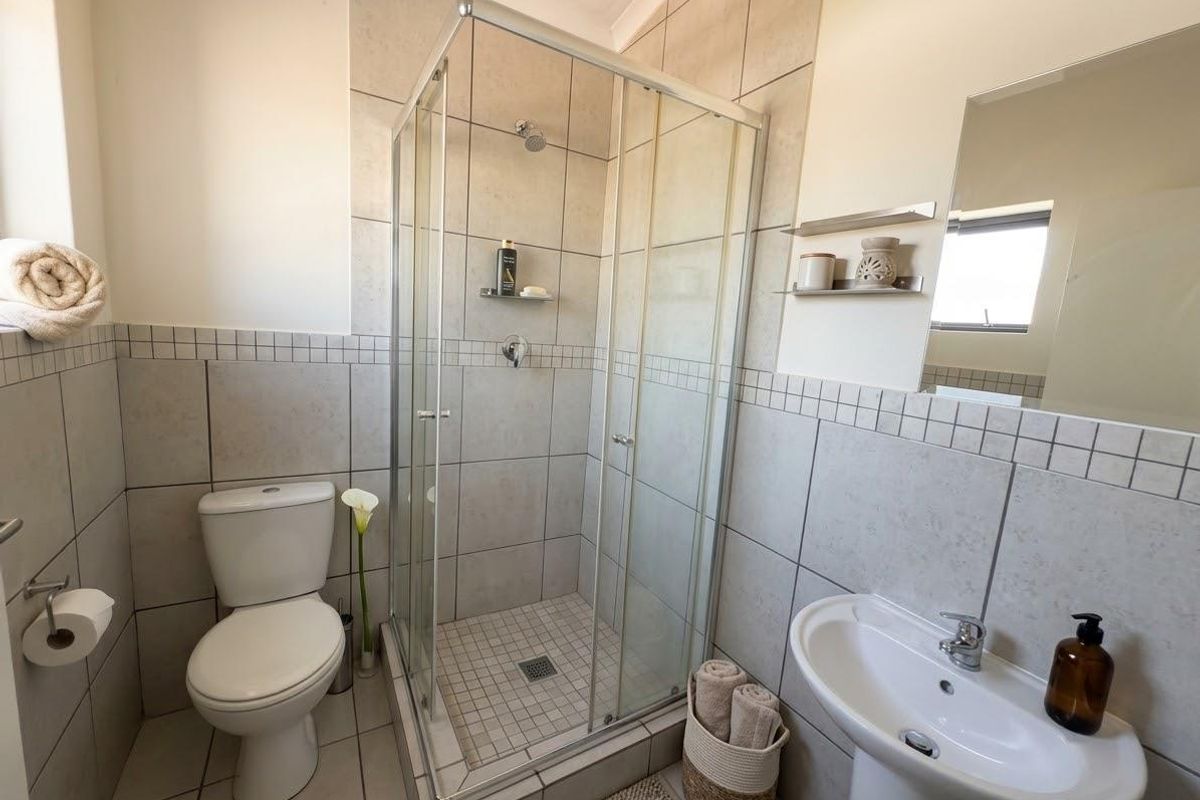 A clean and functional bathroom featuring a glass shower enclosure, pedestal basin, toilet, and neutral wall tiling.