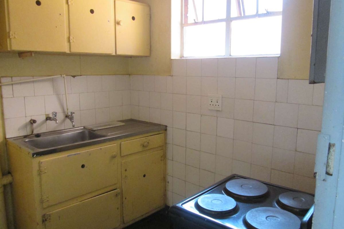 A dated kitchen featuring original cabinetry, a stainless steel sink, and tiled splashbacks, offering significant potential for a modern renovation.