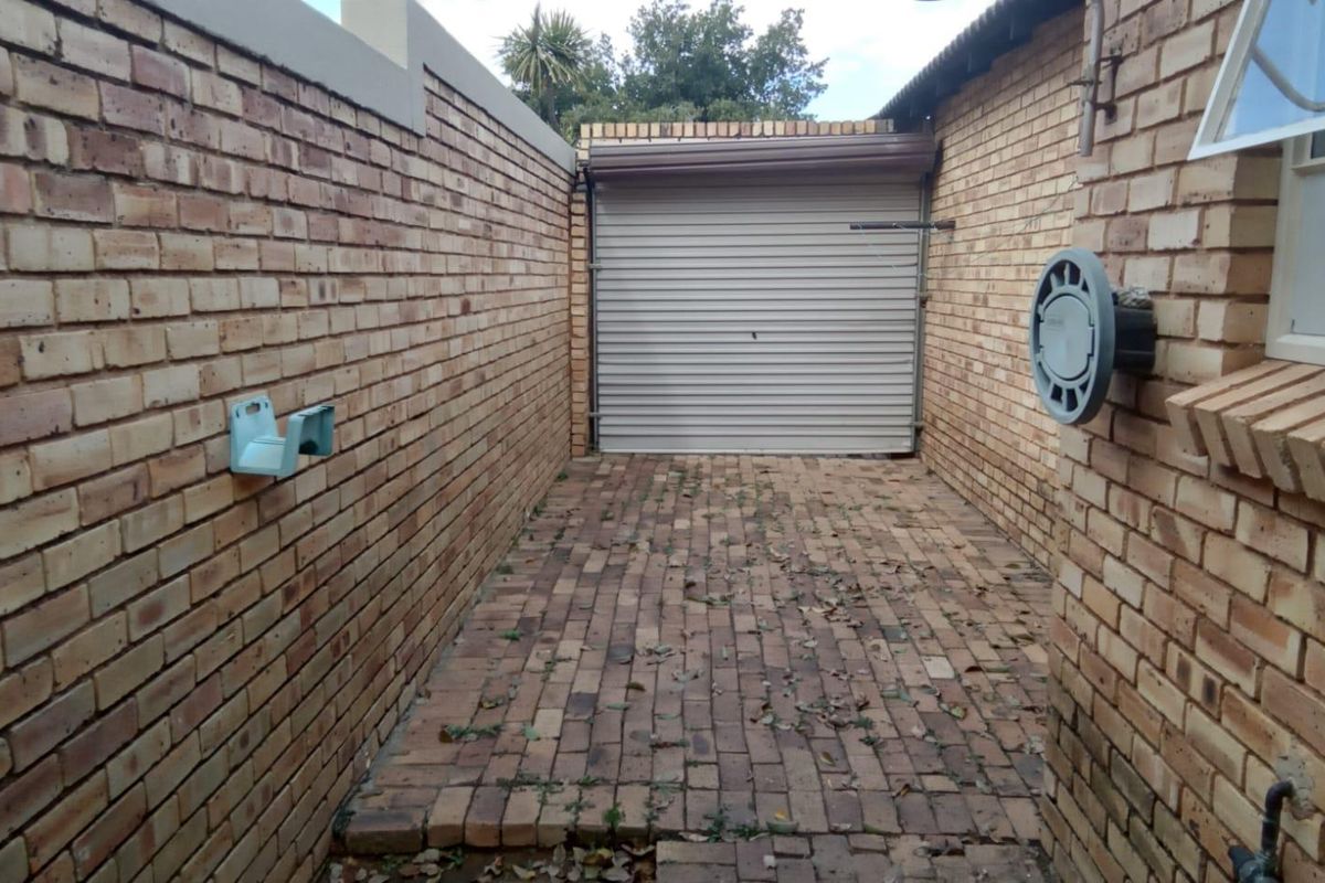 A narrow exterior side passage featuring face-brick walls, paved flooring, and a roller shutter garage door.