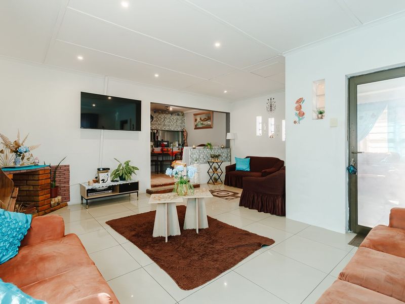 Spacious living room featuring tiled flooring, recessed downlighting, and a brick fireplace, with an open-plan flow leading into the adjacent kitchen area.