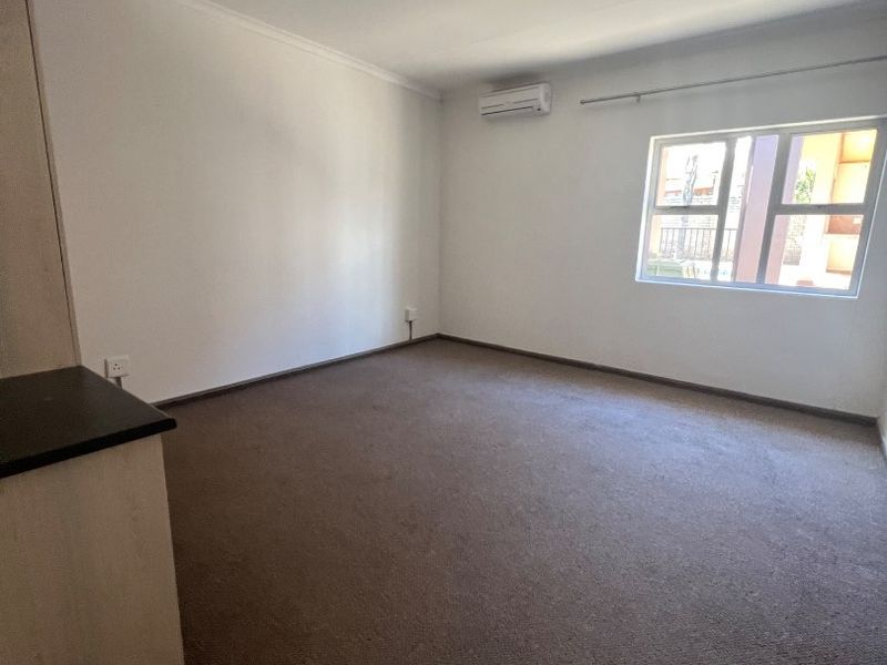 A spacious, empty bedroom featuring neutral walls, carpeted flooring, built-in cabinetry, and a wall-mounted air conditioning unit.