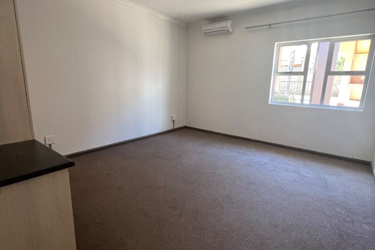 A spacious, empty bedroom featuring neutral walls, carpeted flooring, built-in cabinetry, and a wall-mounted air conditioning unit.