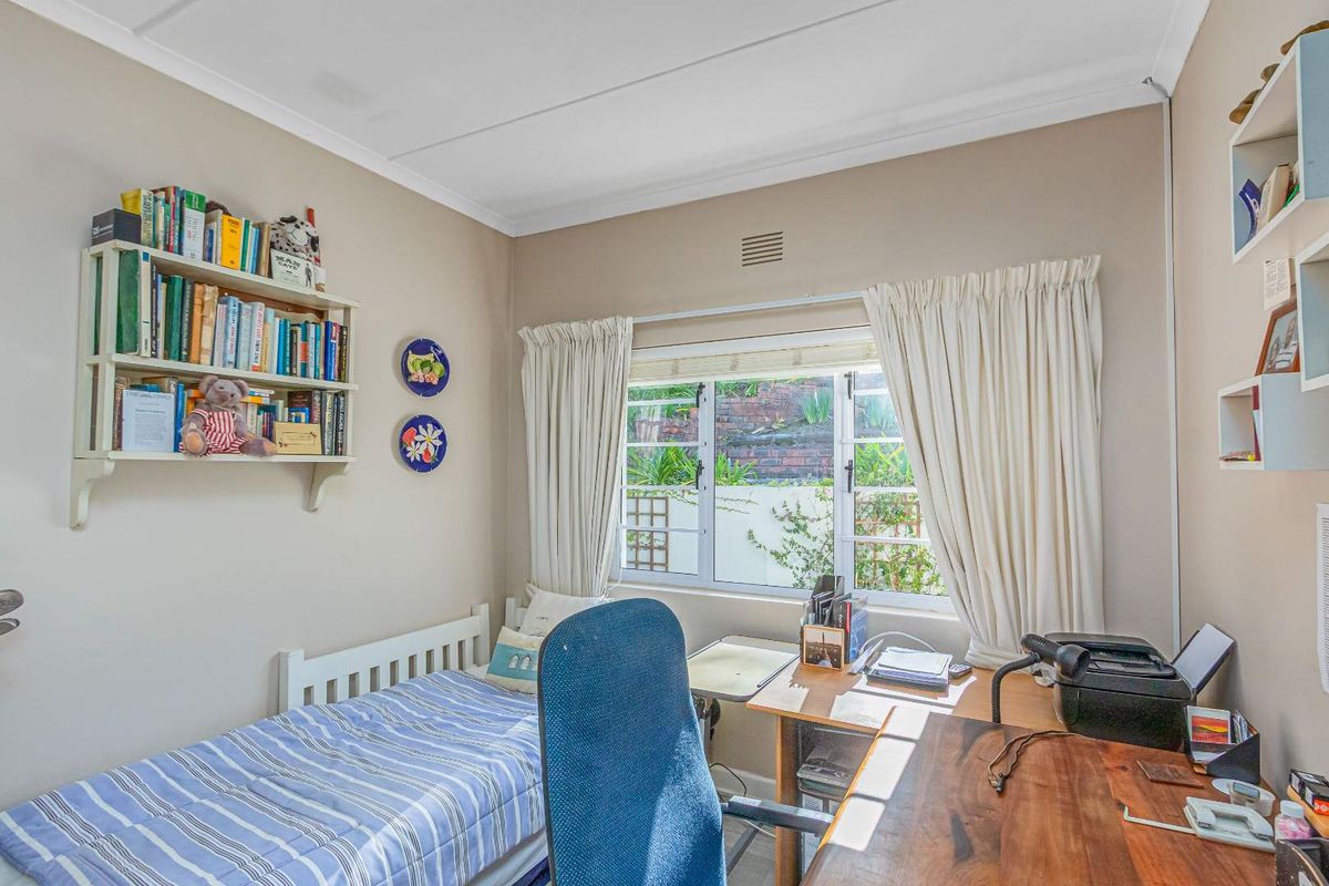 A functional bedroom featuring a window with garden views, built-in shelving, and neutral wall finishes.