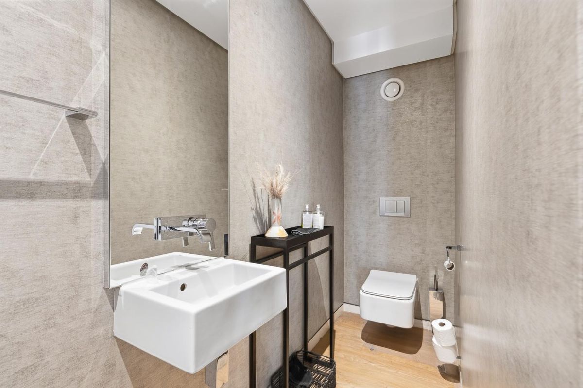 Modern guest bathroom featuring a wall-mounted basin, wall-mounted toilet, large mirror, and neutral textured wall finishes.