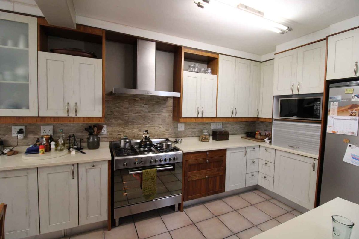 A functional kitchen featuring built-in cabinetry, a stainless steel gas stove with extractor fan, tiled backsplash, and tiled flooring.