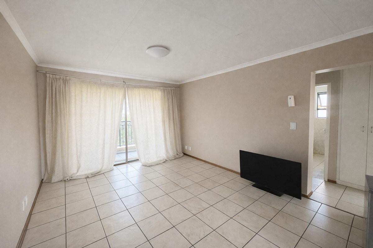 A bright, open-plan living area featuring neutral tiled flooring, sliding glass doors leading to a balcony, and access to an adjoining room.
