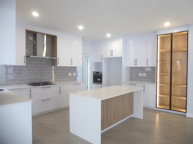 Modern kitchen featuring white cabinetry, a central island with timber detailing, quartz countertops, subway tile backsplash, and integrated lighting.