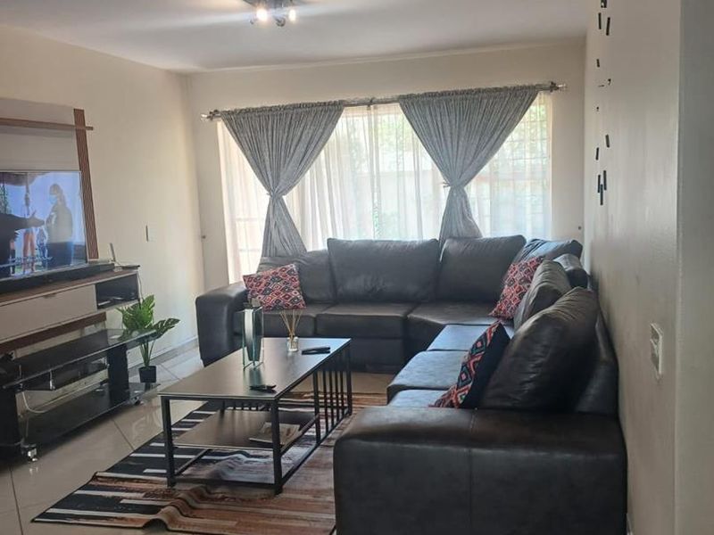 A comfortable living room featuring neutral tiled flooring and natural light through large windows, providing a functional and inviting space for relaxation.