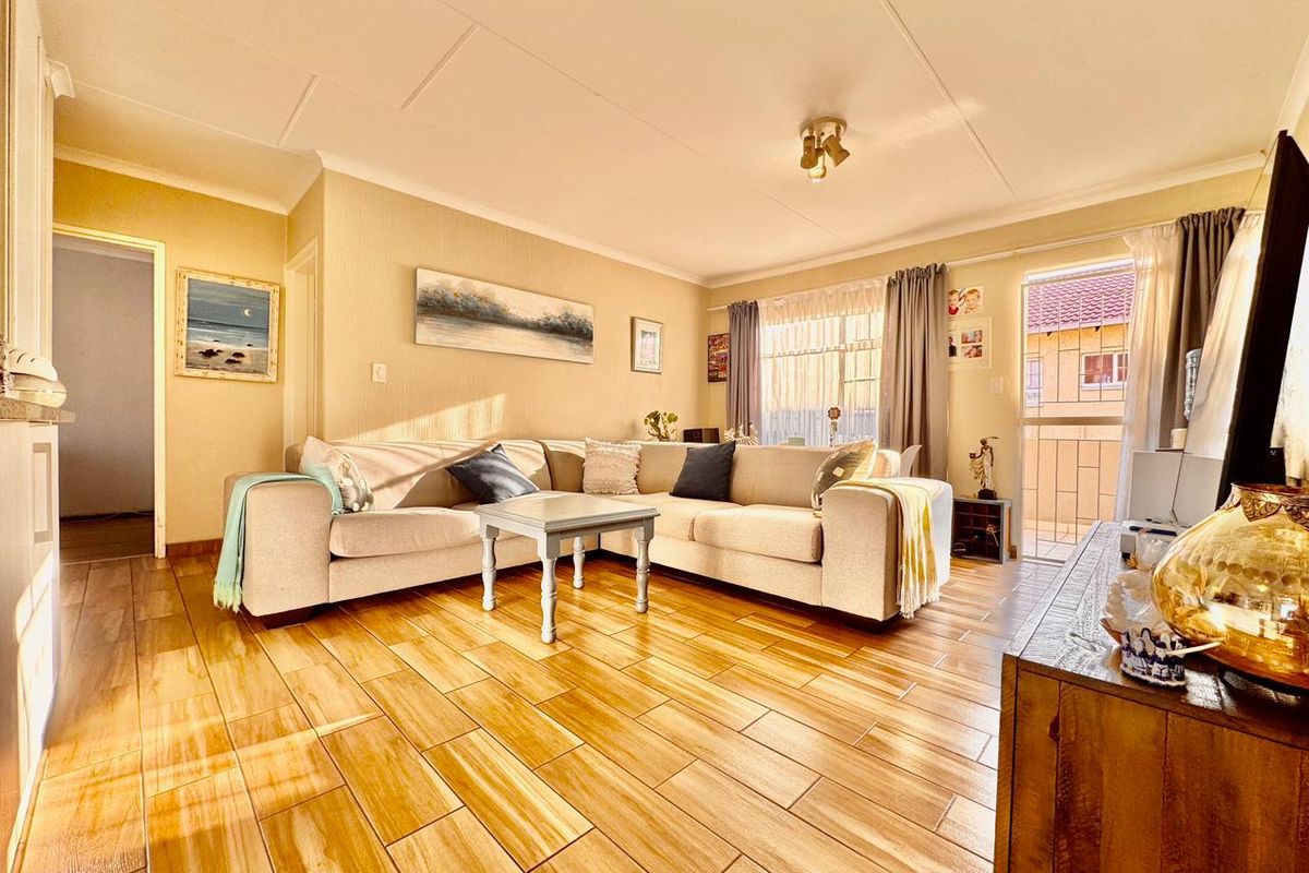 A well-lit living room featuring wood-look tiled flooring and a sliding glass door providing access to an outdoor balcony area.